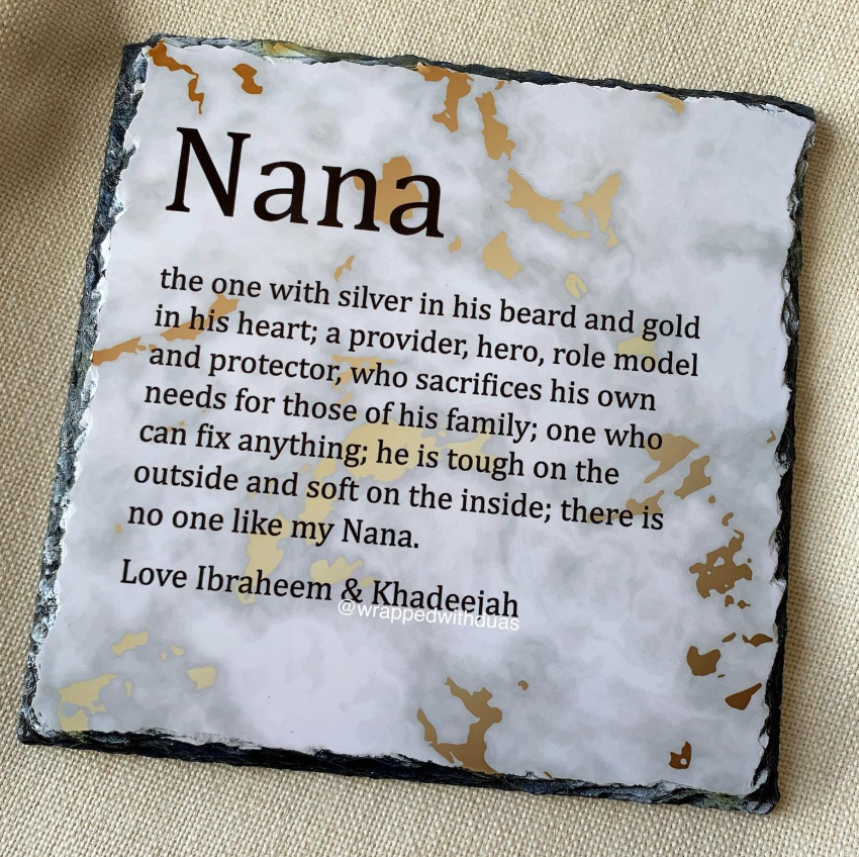 Personalized square slate plaque with a black textured border, featuring a white marbled center printed with a loving tribute poem to 'Nana' by Ibraheem & Khadeejah. The plaque is photographed flat on a beige woven fabric background.