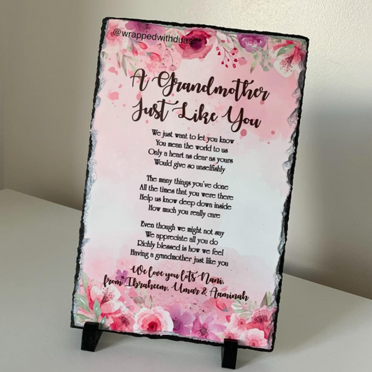 A rectangular slate sign with a black slate border, featuring a pink floral design and a sentimental poem titled 'A Grandmother Just Like You'. The sign is displayed on a small black stand against a neutral beige background.