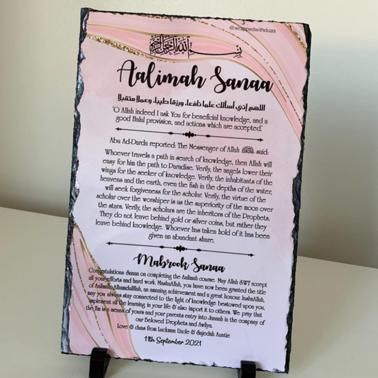 A pink Islamic wedding invitation card with gold foil accents and black text, photographed against a neutral light gray background.