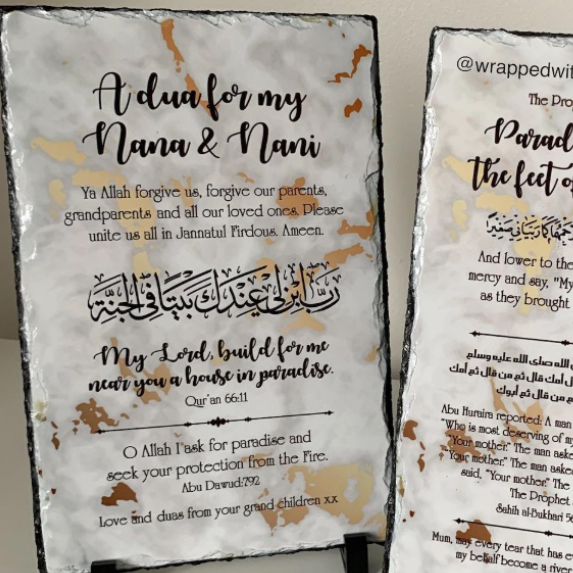 Two rectangular memorial-style plaques with a white and gray marbled background and brown/gold veining, displayed on small black stands against a light wall. One plaque reads 'Adua for my Nana & Nani' with Arabic calligraphy and English prayer text.