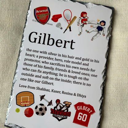 A personalized black slate plaque featuring a custom sports-themed memory quote for 'Gilbert' with various sports logos and illustrations, photographed on a beige textured fabric background.