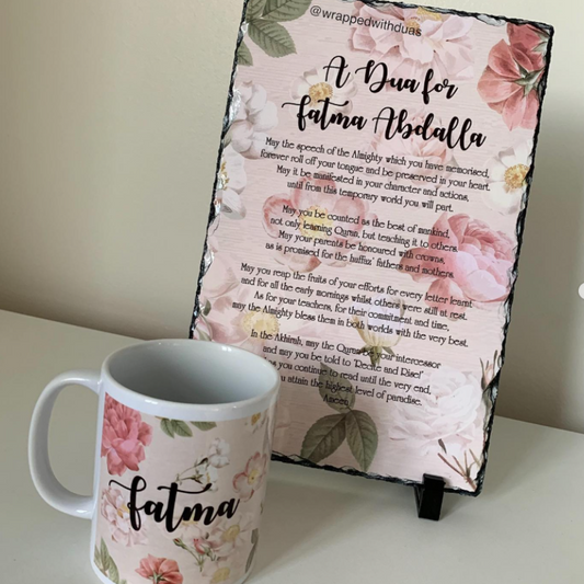 A floral printed slate sign with Arabic and English text reading 'A Dua for Fatma Abdalla' is displayed on a shelf next to a white ceramic mug with matching pink floral print and the word 'Fatma' in black script.