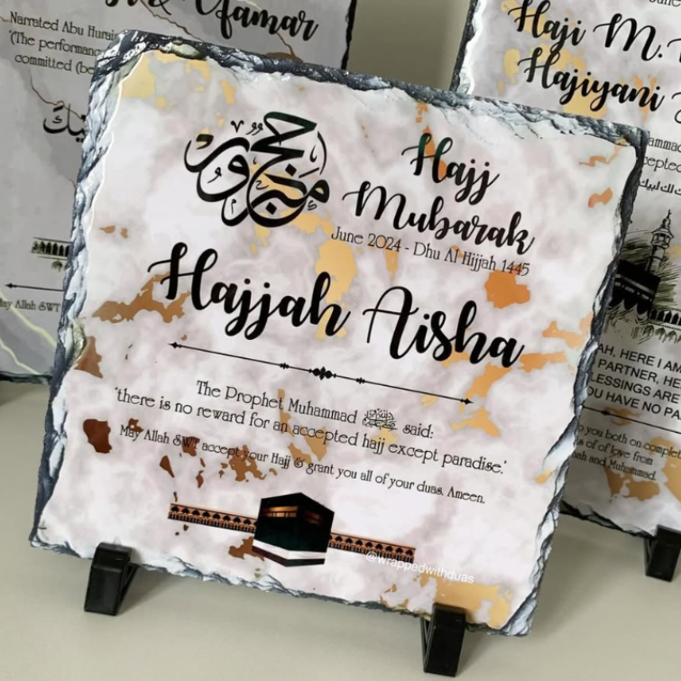 A square slate plaque with natural rough edges, printed with Islamic wedding calligraphy and quotes, displayed on small black stands. Other similar plaques are partially visible in the background.