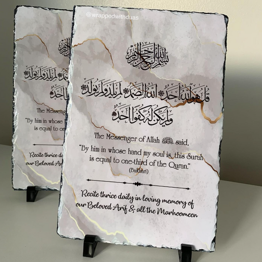 Two rectangular slate wall plaques on small black display stands, featuring Arabic calligraphy, a quote from the Quran, and a prayer text on a light marble-look surface with subtle gold veining.