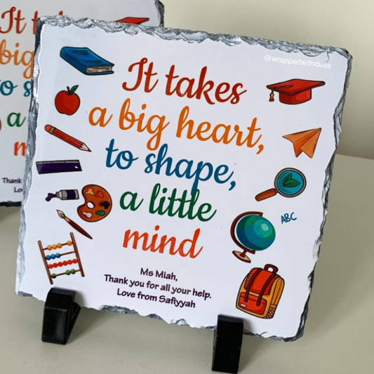 Personalized square slate sign on a black display stand, featuring colorful school-themed illustrations and the message 'It takes a big heart, to shape, a little mind' with the name 'Ms. Miah'.
