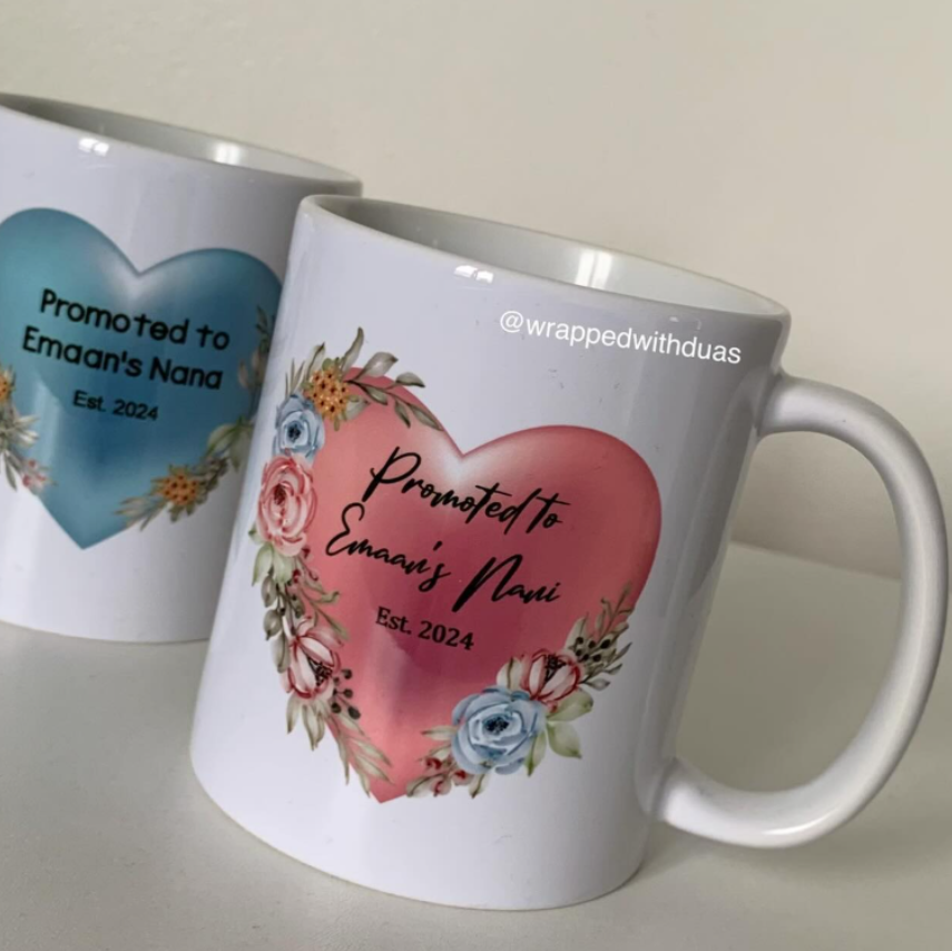 Two white ceramic mugs with custom printed heart designs and floral accents, photographed on a light neutral surface against a soft beige background.