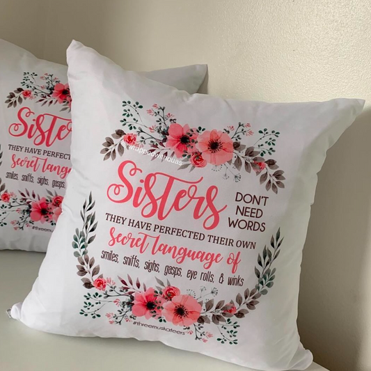 A square white cushion with a floral design and the word 'Sisters' in pink.