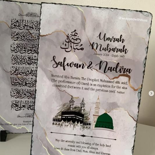 Personalized Islamic wedding anniversary slate plaque with 'Umrah Mubarak' and 'Salwan & Nadira' text, mosque illustration, and gold veining on a white marble-look surface, displayed on small black stands.