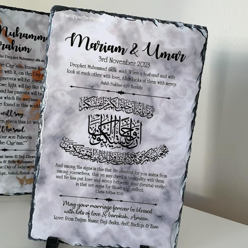 A rectangular slate wedding keepsake plaque with a dark textured border, featuring personalized Islamic wedding text and calligraphy in black on a white stone-like surface. A second plaque is partially visible behind it on a light wall.
